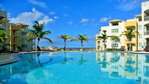 A clear blue pool surrounded by palm trees and multi-story buildings with balconies. - Beachfront Modern Loft with Large Private Terrace (Isabela)