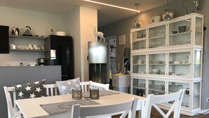 Un comedor con una mesa y sillas blancas, un armario blanco con puertas de cristal y una cocina al fondo.