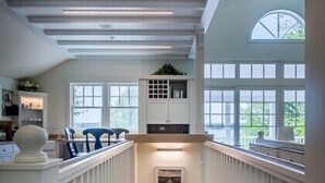 Een meerlaags interieur met een centrale trap, houten leuningen en grote ramen voor natuurlijk licht.
