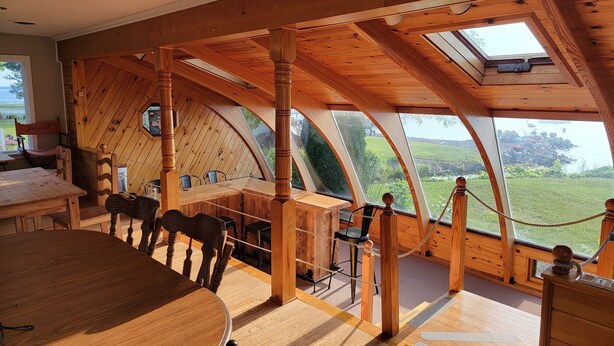 Um interior de madeira aconchegante com uma grande mesa redonda e cadeiras, teto alto com claraboias e vista para o exterior.