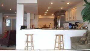Cozinha moderna com ilha central, banquetas de bar e uma grande planta em vaso.