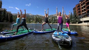 Eine Gruppe von Menschen steht auf Paddleboards auf dem Wasser, mit Bergen im Hintergrund.