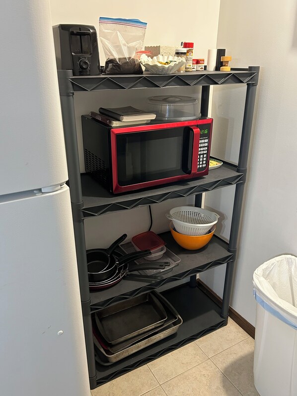 A kitchen with a microwave on a black shelf, a trash bin, and various kitchen items. - Cozy Lakeside Retreat (Lake View)