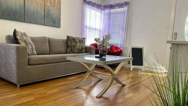 Een woonkamer met een bank, een salontafel met glazen blad en een rode poef.