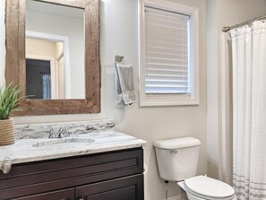A bathroom with a marble sink, a wooden-framed mirror, a toilet, and a window with blinds. - Memory Lane with Community Pool! (Laconia)