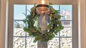 A kitchen with a hanging light fixture, a window with a view of rocks and an American flag, and a countertop with a bottle and a towel. - Memory Lane with Community Pool! (Laconia)