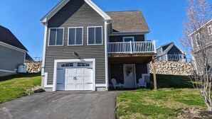 A two-story house with a garage, a balcony, and a stone retaining wall. - Memory Lane with Community Pool! (Laconia)