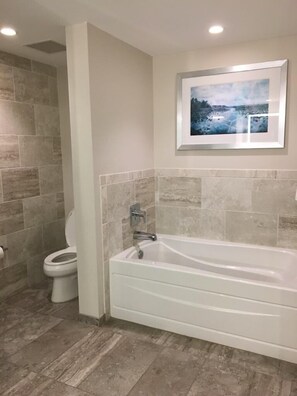 Bathroom features a bathtub and toilet, surrounded by neutral-toned tiles.