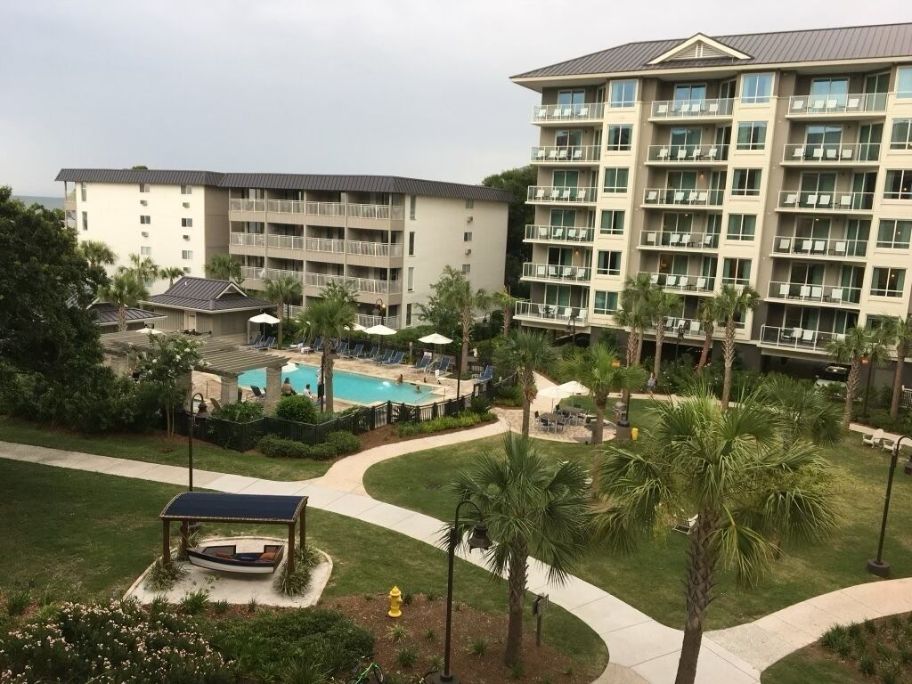 A hotel with multiple floors, a swimming pool, and a well-maintained lawn with palm trees.