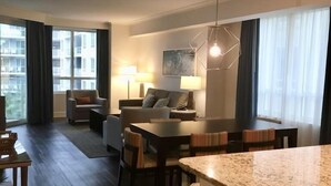 A modern hotel room with a dining area, a sofa, and a large window with curtains. - OCEAN FRONT, PRIVATE BEACH Luxury Suite with Balcony sleeping 8 adults (Hilton Head Island)