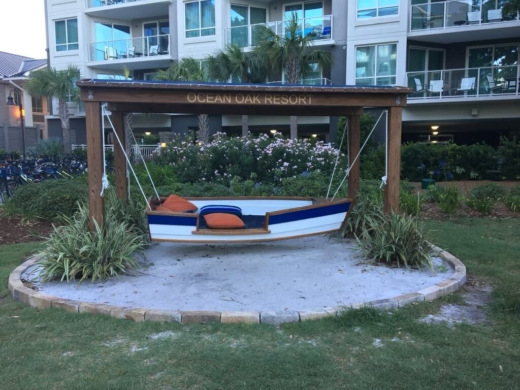 Una poltrona a dondolo in legno con decorazioni blu e bianche, con la scritta "OCEAN OAK RESORT", di fronte a un edificio con balconi e finestre.