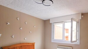 A bedroom with a wooden bed, a white radiator, a ceiling fan, and a window with an open shutter.