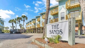A beachfront hotel named "The Sands" with a signboard, palm trees, and a clear sky.