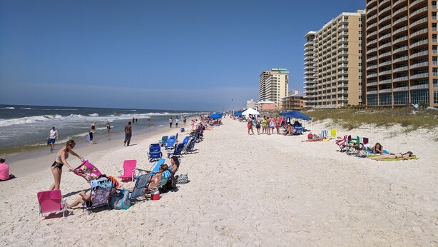 A beach with rows of beach chairs and umbrellas, a tall hotel building, and the ocean in the background.