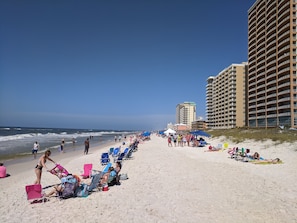Ein Strand mit Reihen von Liegestühlen und Sonnenschirmen, ein hohes Hotelgebäude und das Meer im Hintergrund.