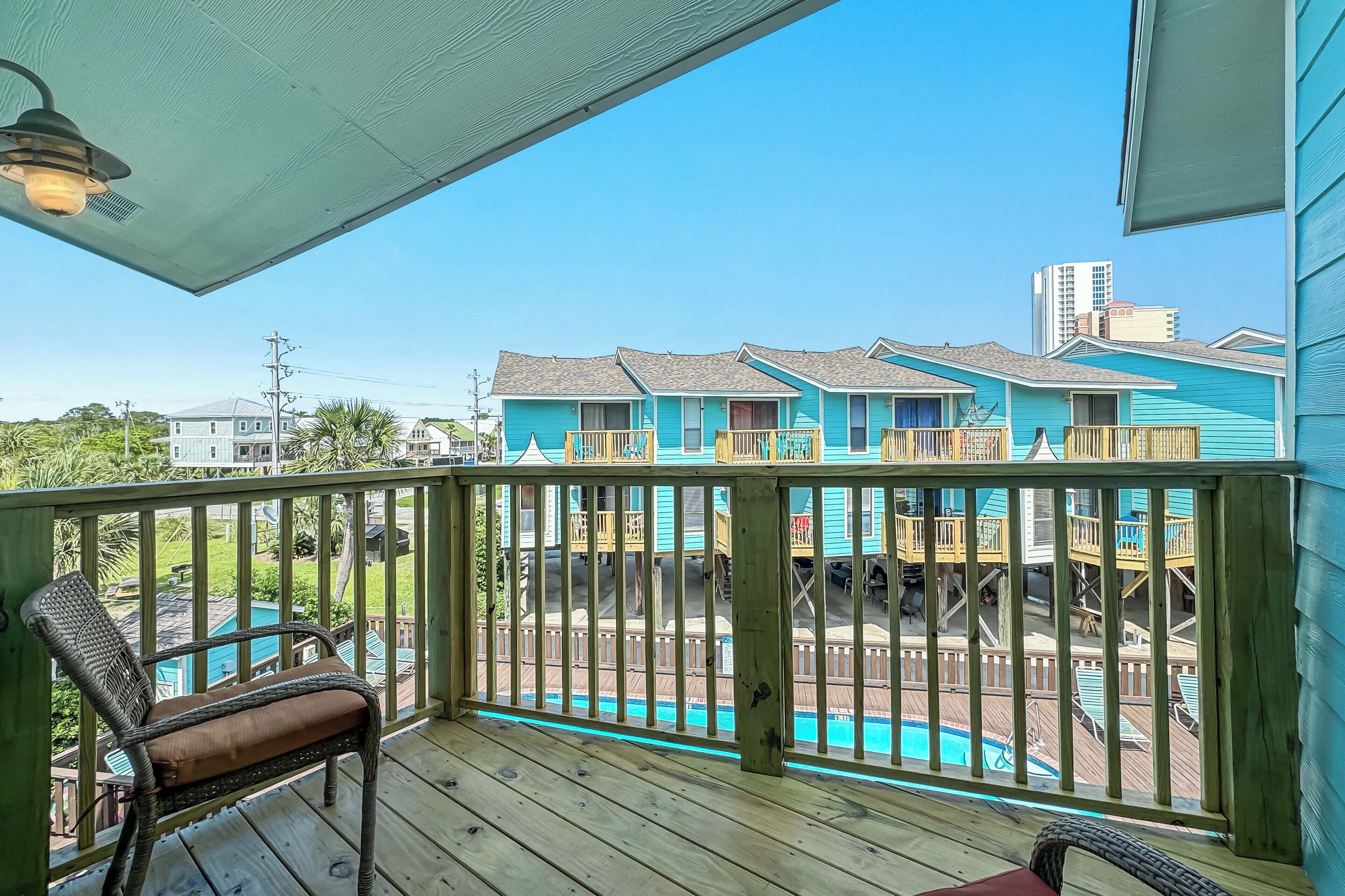 A wooden deck with a pool, blue buildings in the background, and a clear sky.
