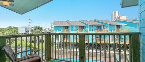 A wooden deck with a pool, blue buildings in the background, and a clear sky.