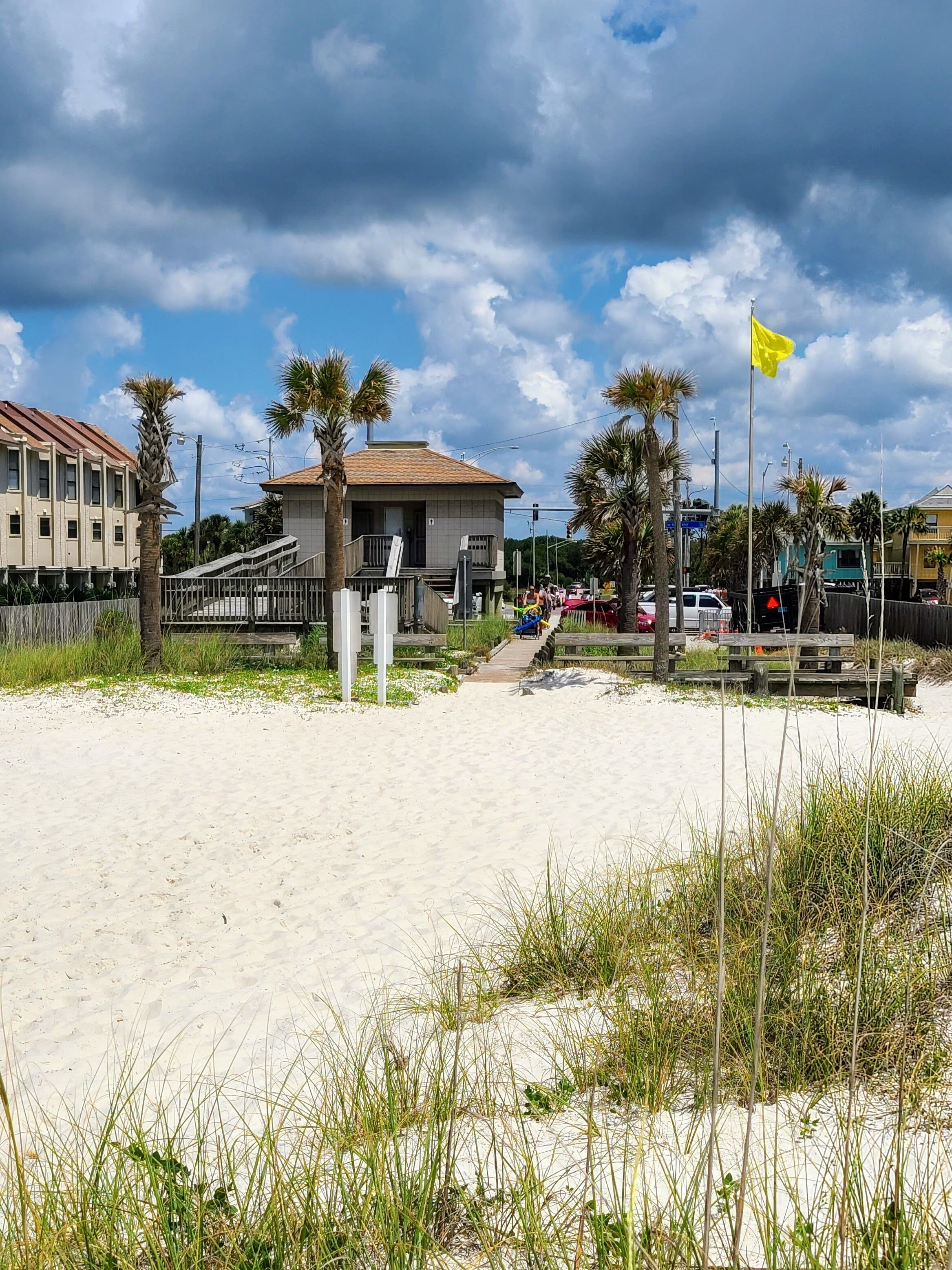 A beach with a wooden walkway leading to a building with a tiled roof.