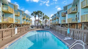 A pool area with wooden deck, poolside chairs, and a clear blue sky.