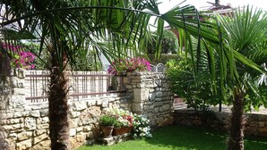 Un muro de piedra con una reja de metal, rodeado de césped verde exuberante y plantas en flor.