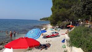 Una playa con gente nadando y tomando el sol, sombrillas y un litoral rocoso.