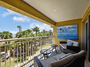 Un balcon avec vue sur les palmiers et l’océan, aménagé avec un canapé, deux fauteuils et une petite table.