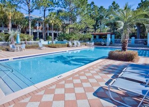 A swimming pool with lounge chairs, palm trees, and a building in the background.