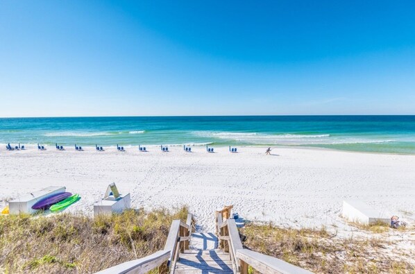 A beach with a wooden walkway leading to the water, a row of beach chairs, and a surfboard.
