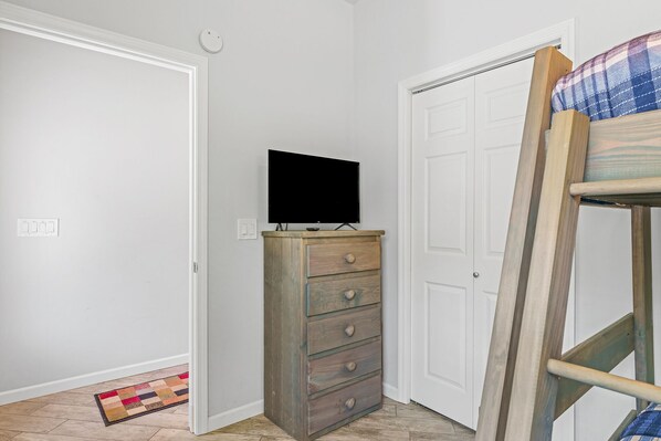 Una habitación con un aparador de madera, un televisor encima, una litera y una puerta.