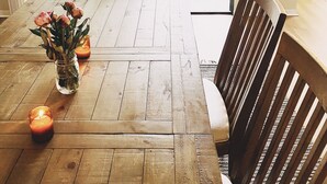 A wooden dining table with a vase of flowers and a candle, set in a room with a view through a glass door to an outdoor patio area.