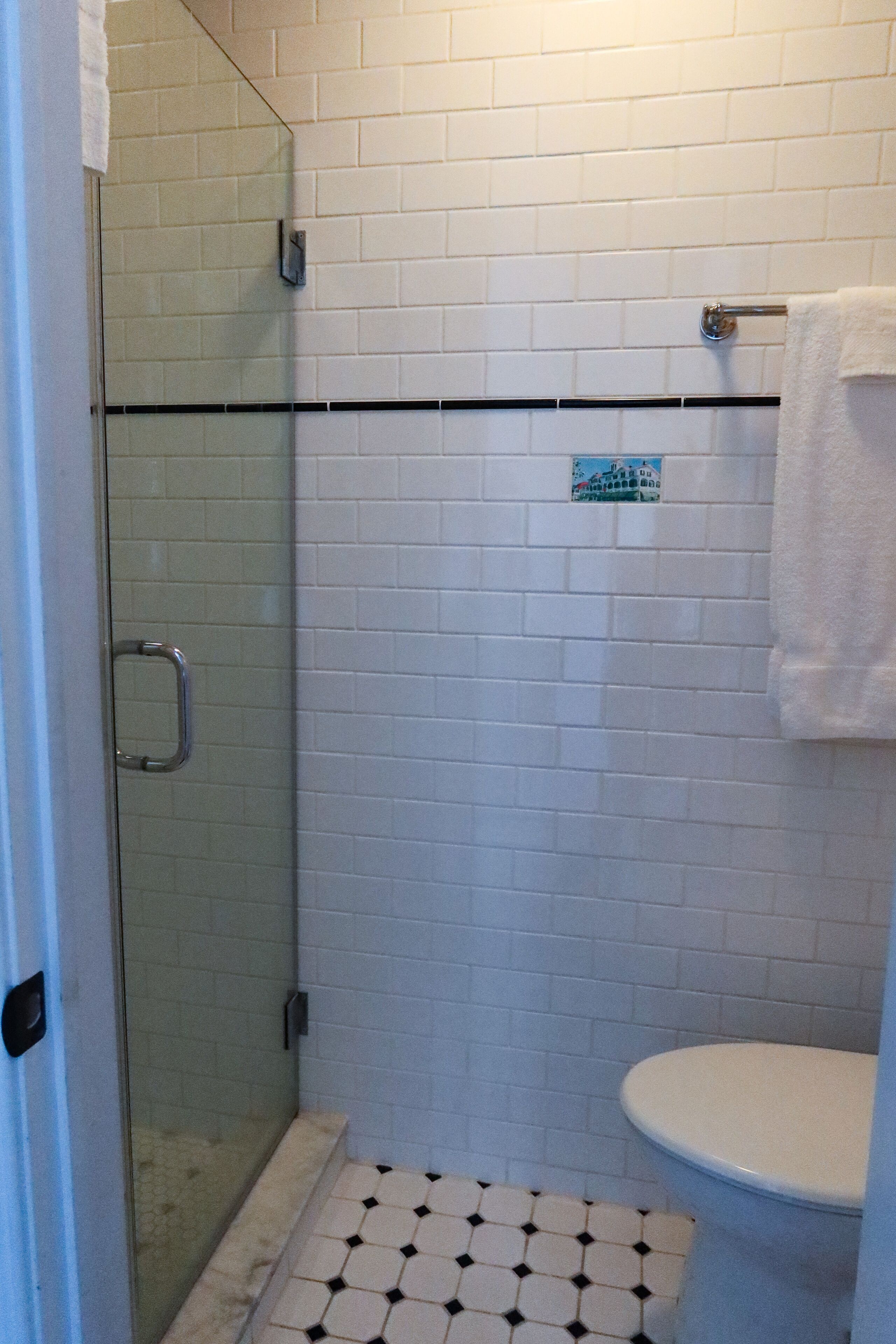 Ein Badezimmer mit einer gläsernen Dusche, weiß gefliesten Wänden, einer weißen Toilette und einem kleinen Schild an der Wand.