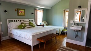 A bedroom with a bed, a bench, a bedside table, a window, and a bathroom with a sink.