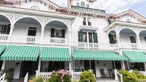 A historic building with a sign reading "Chai Fountain." It features a white facade with green shutters, multiple balconies with ornate railings, and green striped awnings over the entrances.