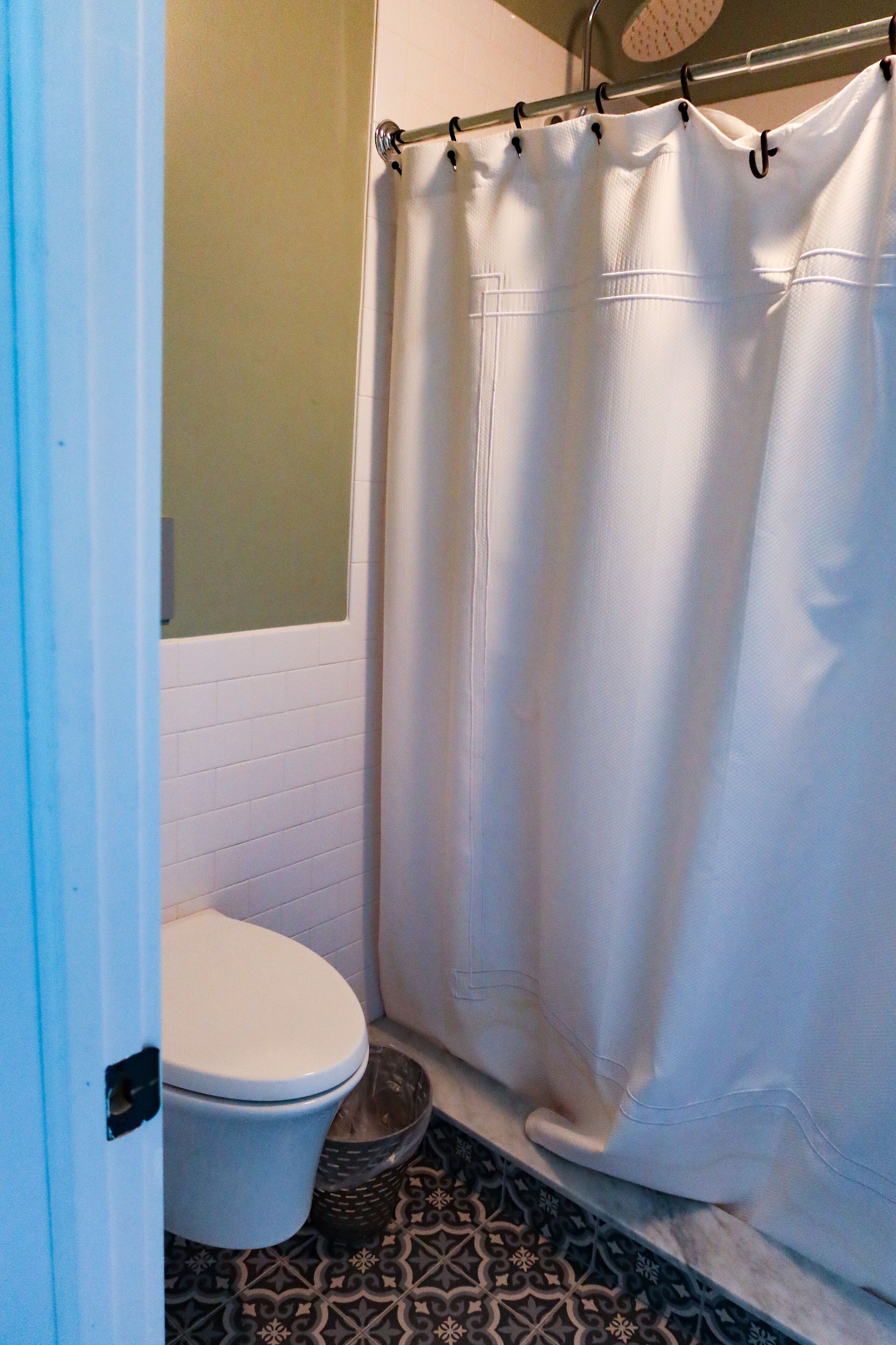 A bathroom with a white toilet, a shower curtain, and patterned floor tiles.