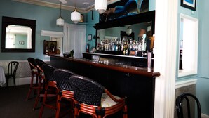 A bar area with wicker chairs, a counter with bottles, and a ceiling fan.