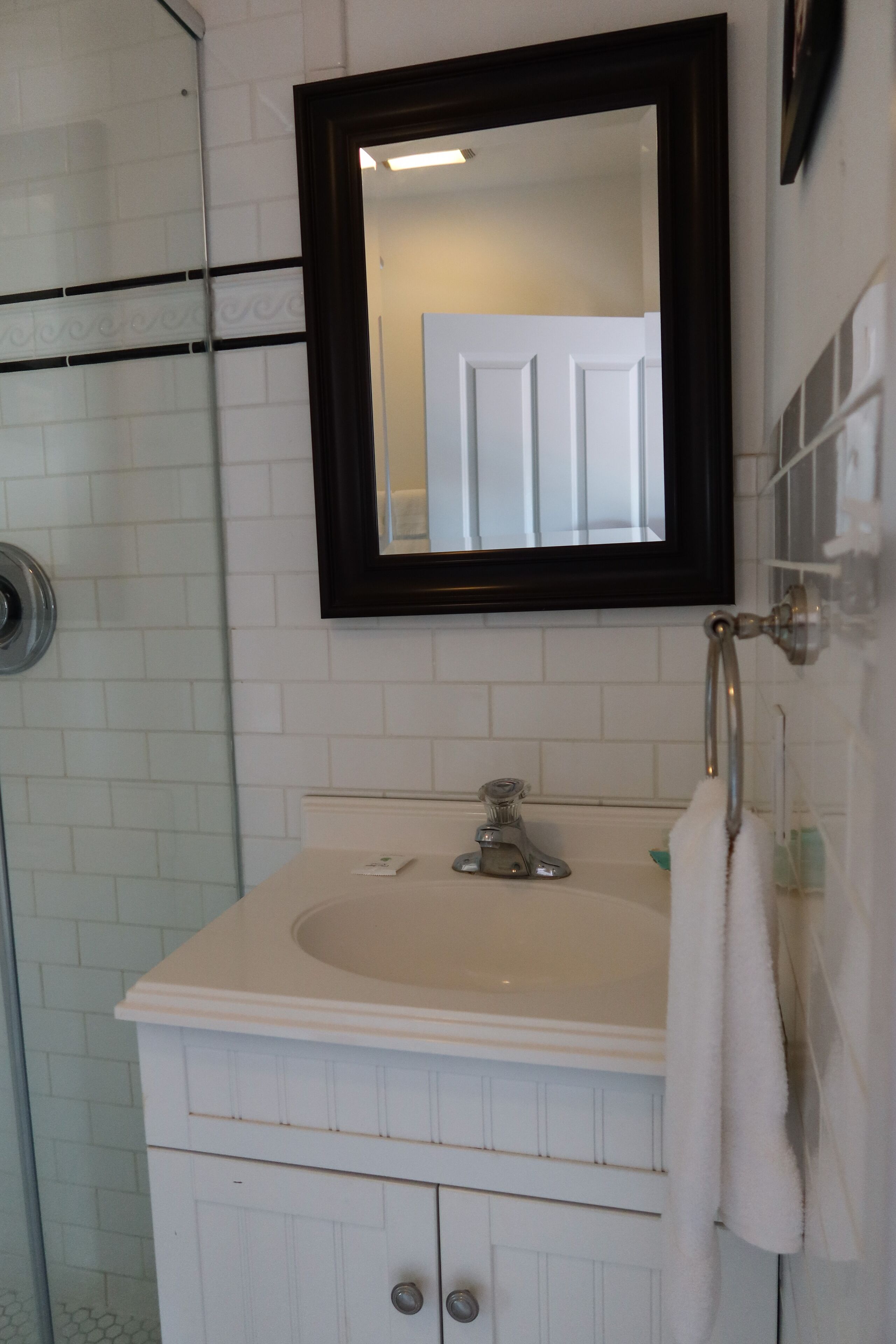 Une salle de bain avec un lavabo blanc, un miroir et une douche en verre.