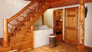 Una escalera de madera que lleva a un área de lavandería con lavadora y un cubo de basura.