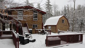 Una cabaña de madera con un porche cubierto, una terraza cercada y un paisaje cubierto de nieve.