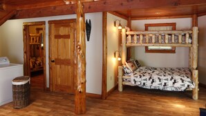 Interior rústico de una cabaña con una cama de madera tipo litera, una lavadora y una cesta de ropa.
