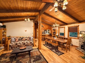 A cozy cabin interior with a wooden ceiling, a dining area, a sofa with patterned cushions, and a fireplace. - Unique Rustic Ski/Tree House - Game room, Hot tub & Sauna (Jay)