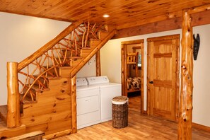 A wooden staircase leading to a laundry area with a washing machine and a basket. - Unique Rustic Ski/Tree House - Game room, Hot tub & Sauna (Jay)