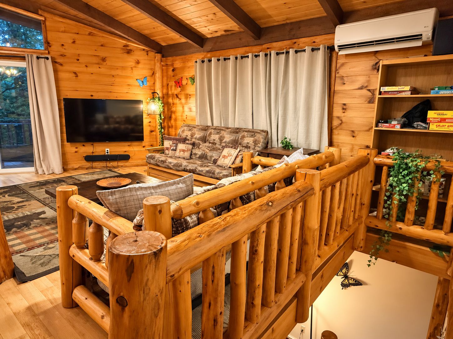 Interior acogedor de una cabaña de troncos con sofá, televisor y barandilla de madera.