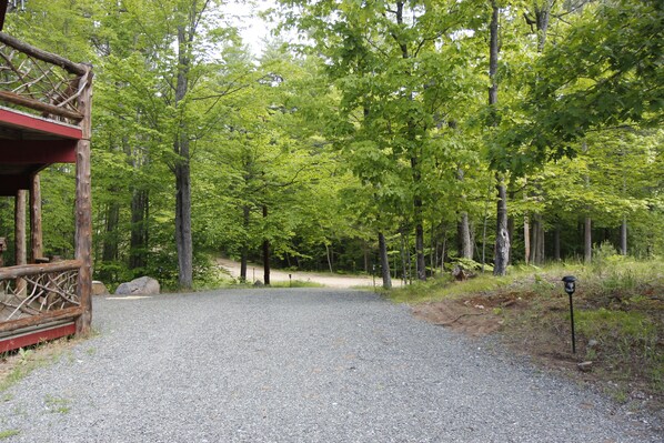 A gravel path leading through a forested area with a wooden structure on the left. - Unique Rustic Ski/Tree House - Game room, Hot tub & Sauna (Jay)