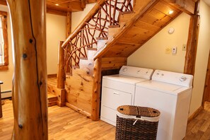 Un espace buanderie équipé de deux machines à laver, d’un escalier en bois et d’un panier à linge en osier.
