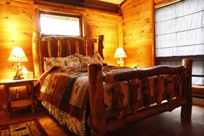 Camera da letto in una baita di legno, con un letto, due lampade sui comodini, una finestra e una testiera in legno.