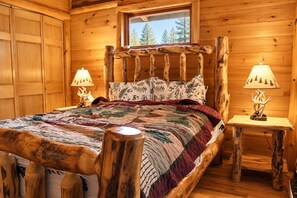 Une chambre dans une cabane en bois, avec un grand lit, deux lampes de chevet et une fenêtre donnant sur la forêt.