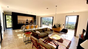 Een ruime woonkamer met een bank, stoelen, een eettafel en een keuken op de achtergrond.