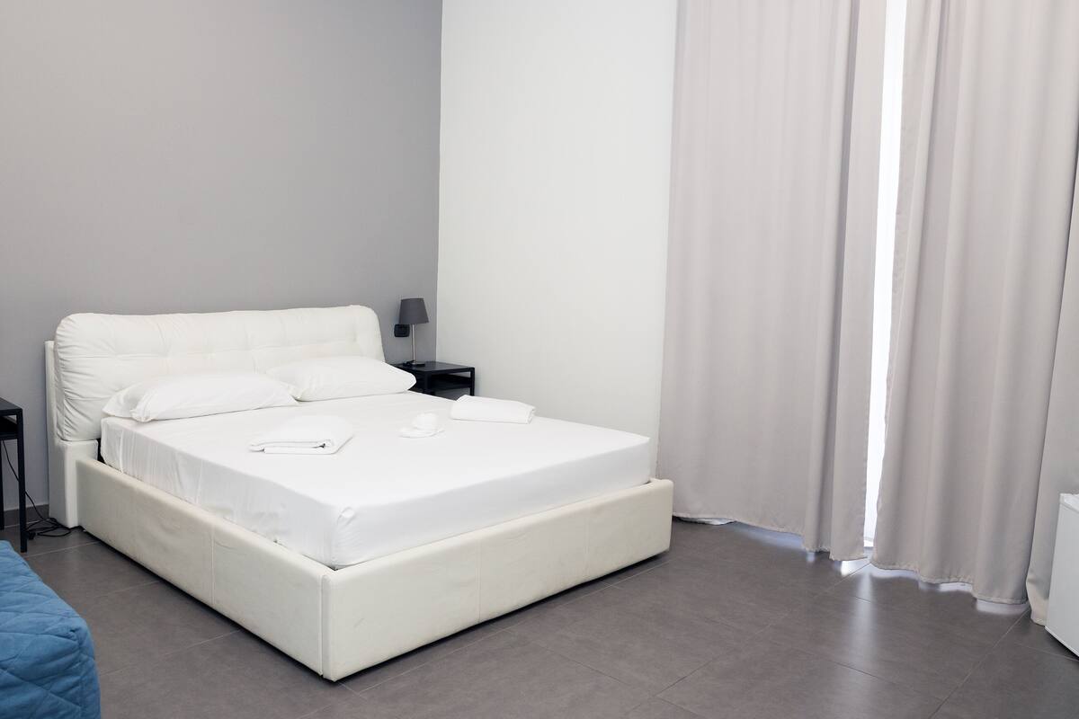 A modern bedroom with a white bed, a bedside table, and a lamp.