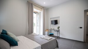 Habitación de hotel moderna con una cama grande, un escritorio, un televisor y una ventana con cortinas.