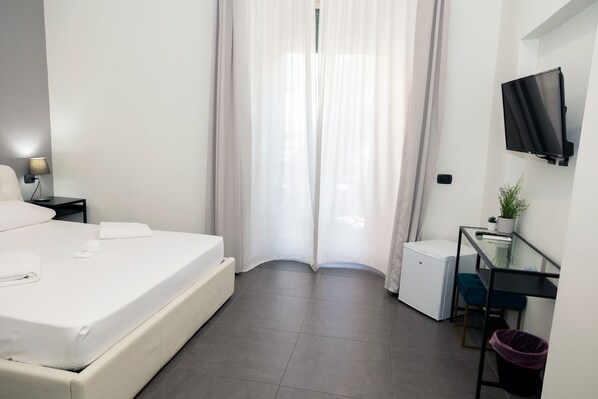 A modern hotel room with a bed, a desk, a TV, and a small fridge. - Doria Suites Napoli (Naples)